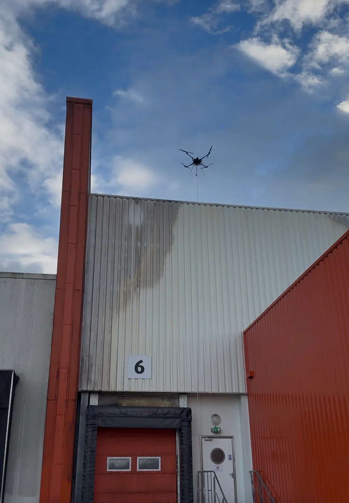Drone en intervention au-dessus d'un bâtiment logistique : nettoyage du bardage encrassé au-dessus des quais de chargement sans arrêter l'activité