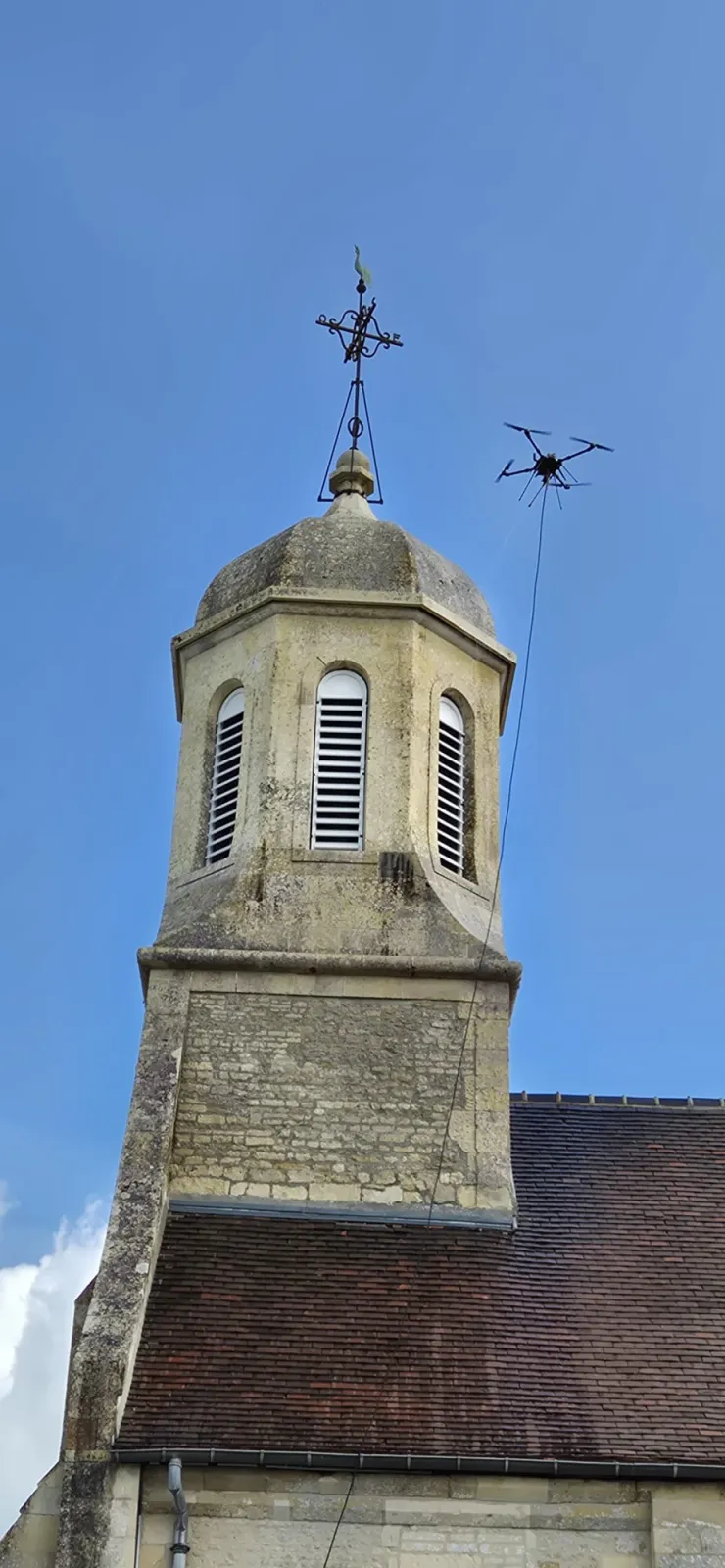 Nettoyage par drone du clocher en pierre d'une église : pulvérisation à distance sous la girouette, sans échafaudage monumental ni contact avec la pierre