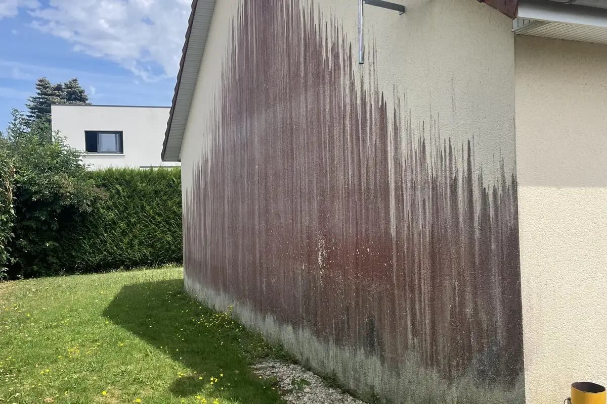 Façade de maison couverte d'algues rouges Trentepohlia dans le Calvados — traces rouge-orangé sur crépi avant nettoyage professionnel