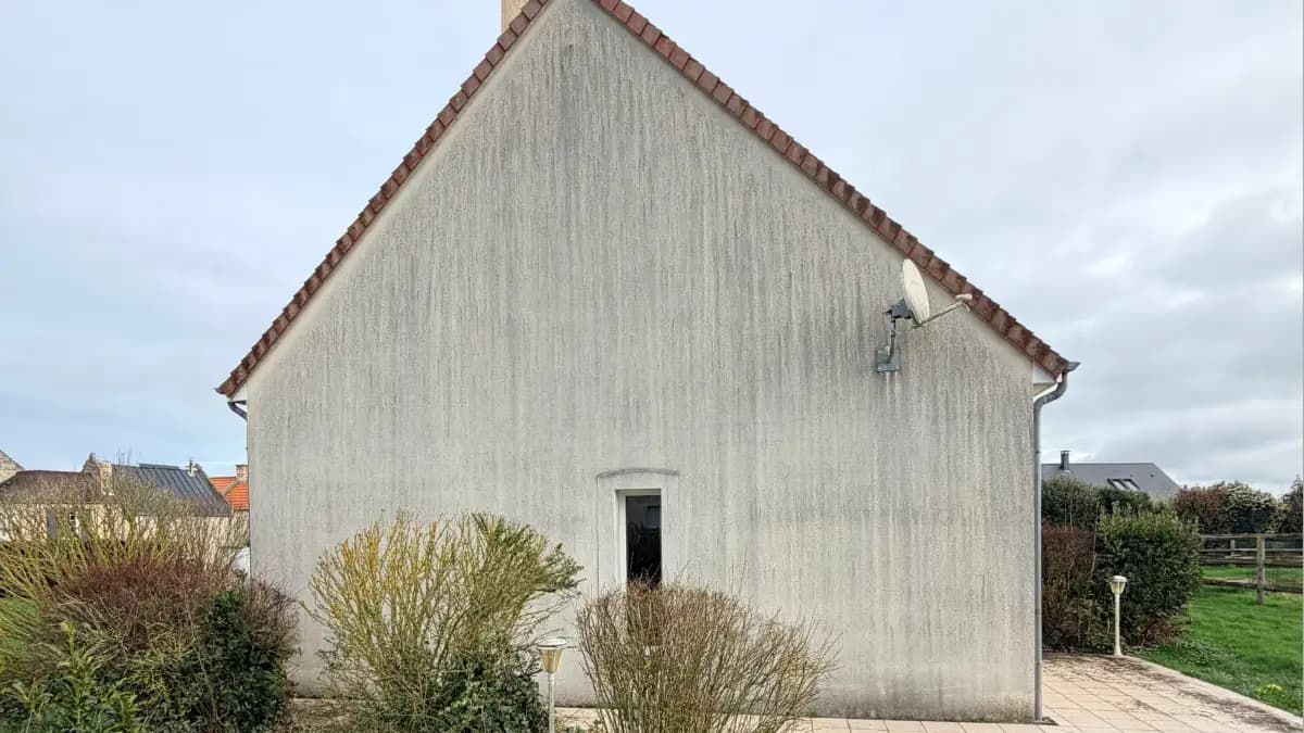 Pignon de maison avec traces noires et coulures sur crépi blanc dans le Calvados