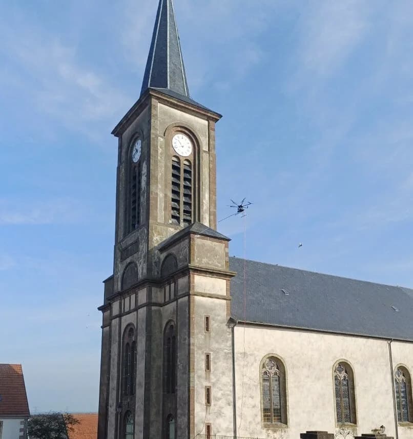 Démoussage du clocher d'une église par drone : traitement pulvérisé à distance sur la pierre, sans contact mécanique ni échafaudage monumental