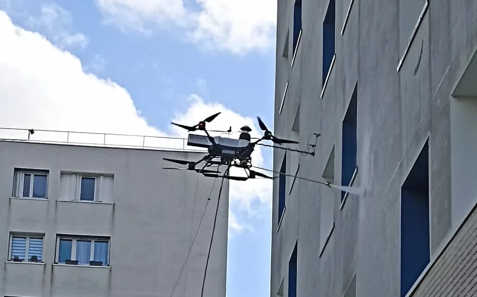 Drone de nettoyage en intervention sur la façade d'un immeuble en copropriété : pulvérisation à distance entre deux bâtiments, sans échafaudage ni nuisance pour les occupants