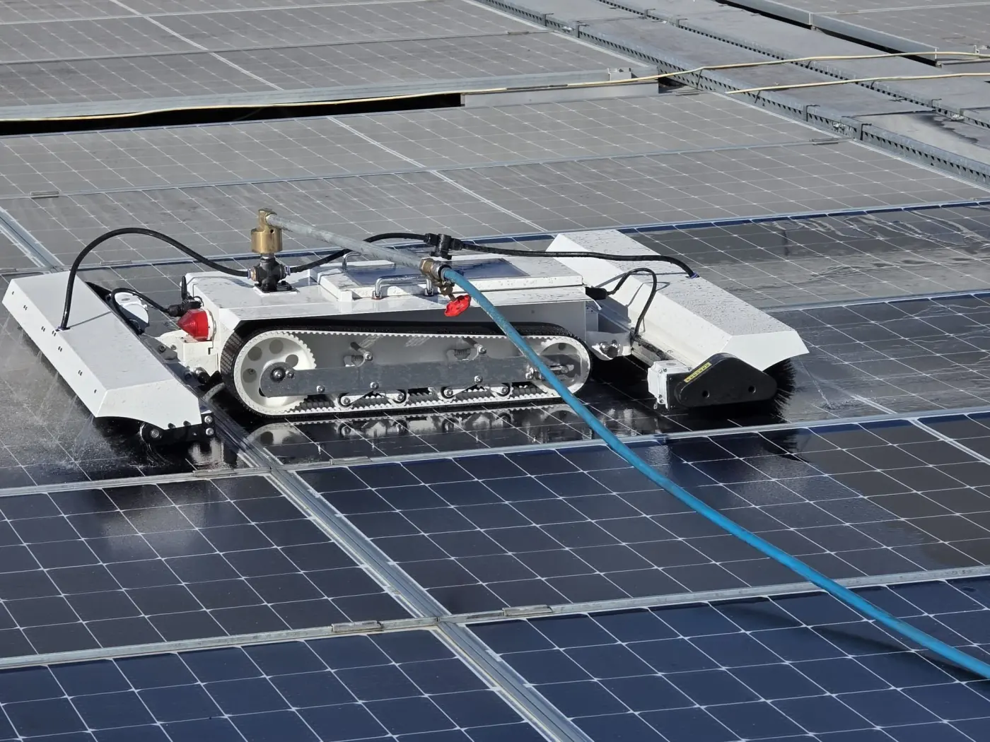 Robot à chenilles souples équipé de brosses rotatives et d'une alimentation en eau pure nettoyant une centrale solaire : idéal fermes photovoltaïques et ombrières