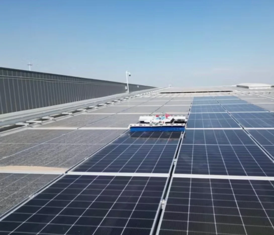 Robot de nettoyage sur une grande toiture photovoltaïque industrielle : les panneaux gris de poussière retrouvent leur couleur d'origine au passage du robot