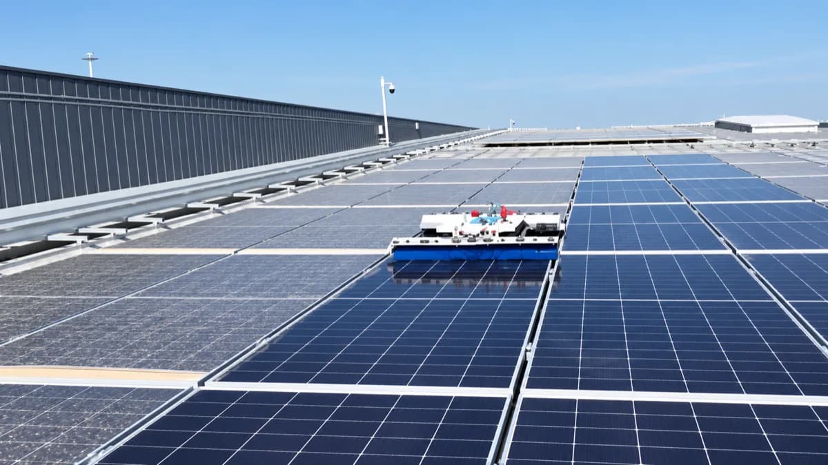 Robot de nettoyage à brosse sur une grande toiture photovoltaïque de hangar : le contraste est net entre les rangées encore voilées de poussière et les panneaux nettoyés d'un bleu profond